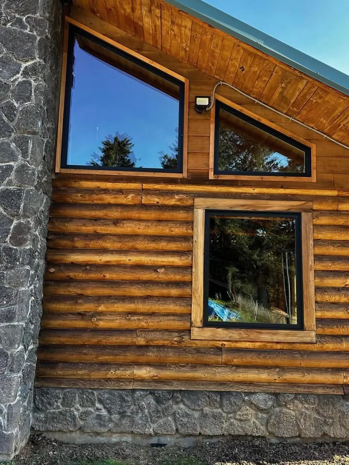 Black-frame trapezoid and picture windows on a log and stone cabin wall