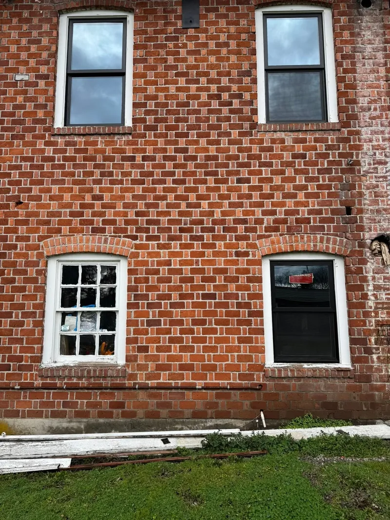New black-frame windows going into a brick wall beside an original divided-lite window, mid-project