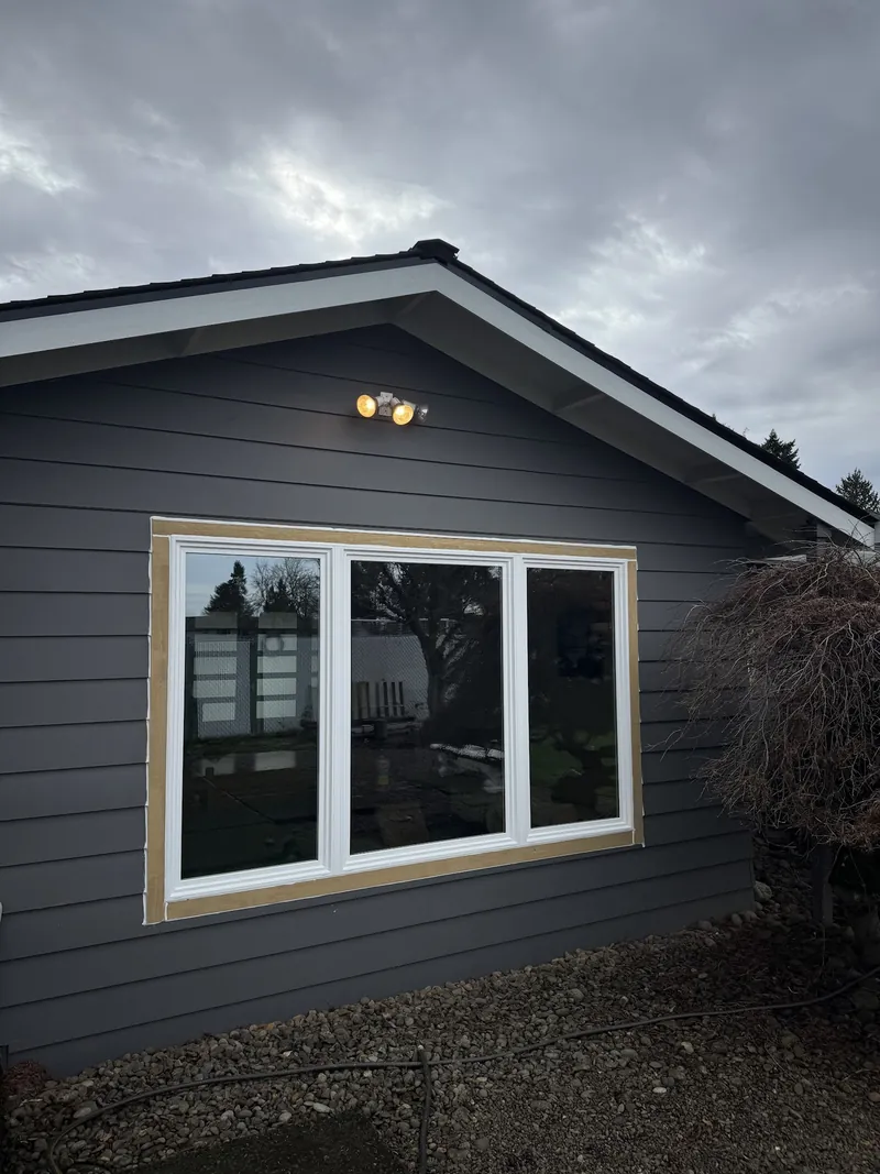 New white triple picture window installed in dark gray lap siding