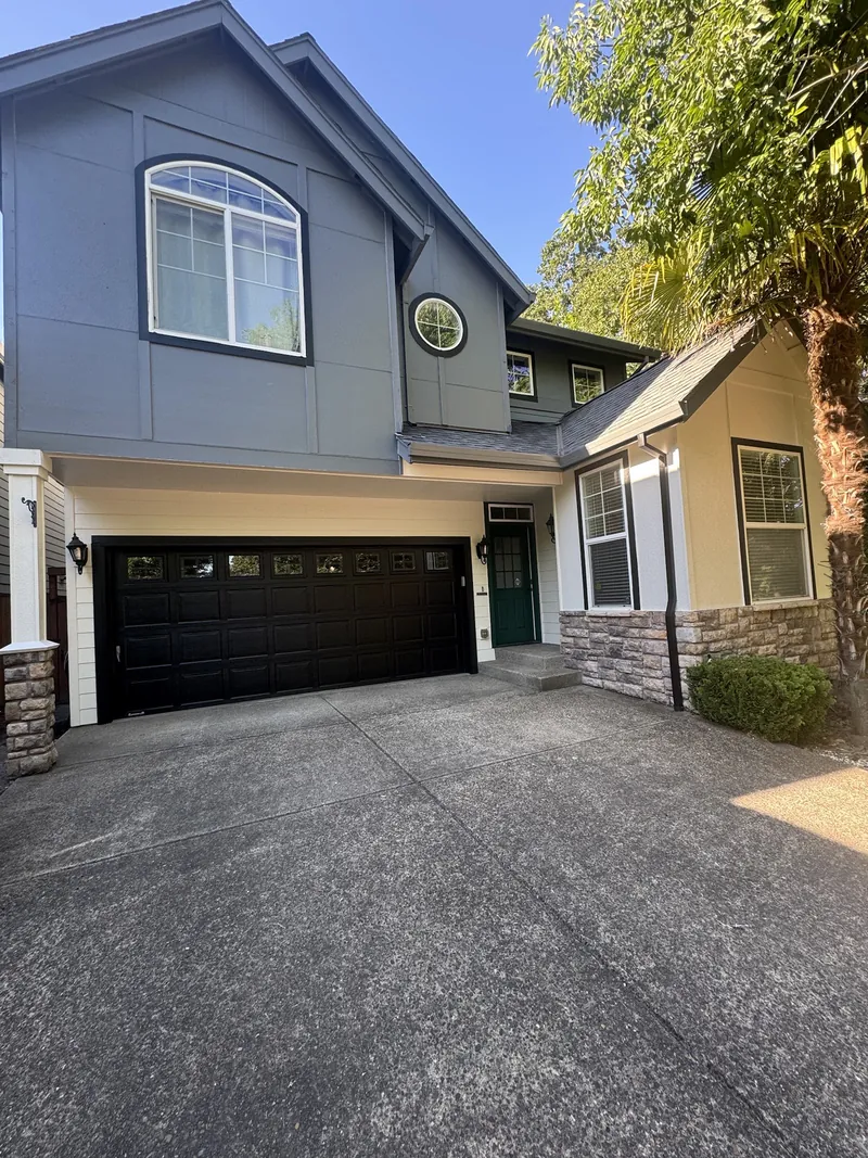 Two-story gray home with new white-trimmed windows, black garage door and stone accents after exterior work